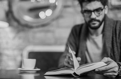 Black and white photo of young man reading a book in coffee shop.